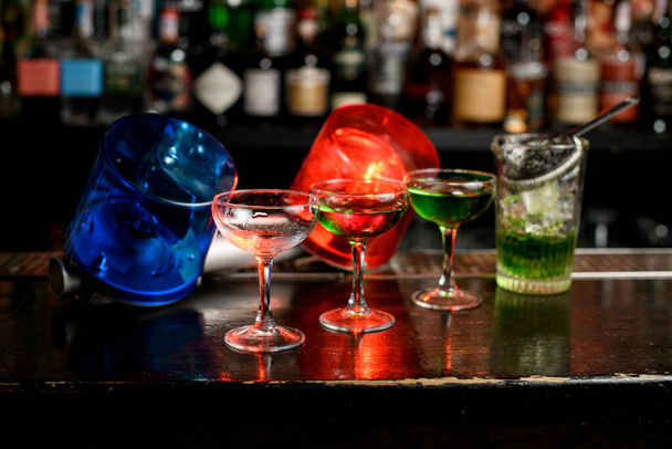 meerdere glazen met groen mengsel staan op bar teller. Blauwe en rode waarschuwingslichten informeren over quarantaine. - Foto, afbeelding