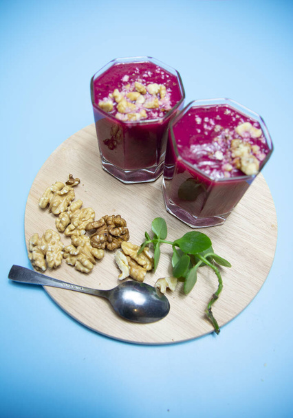 cranberry smoothie on a blue background with slices of nuts. - Zdjęcie, obraz