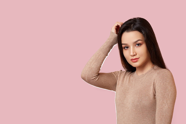 retrato de uma jovem bela menina morena asiática em uma jaqueta marrom claro segurando a cabeça com as mãos. em um fundo isolado rosa com copyspace
. - Foto, Imagem
