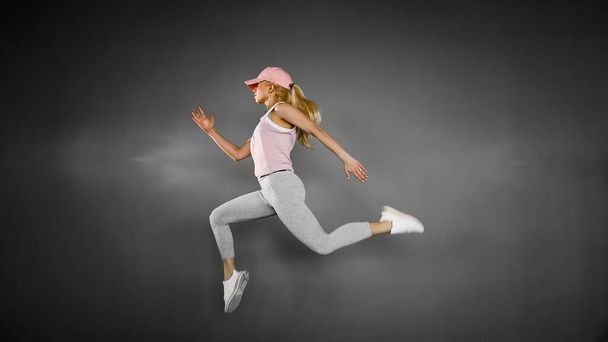 Young woman with fit body jumping and running against grey background. Female model in sportswear exercising - Foto, Imagem