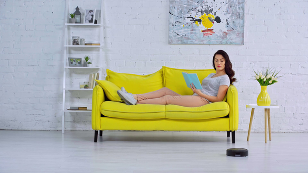 woman reading book near robotic vacuum cleaner - Footage, Video
