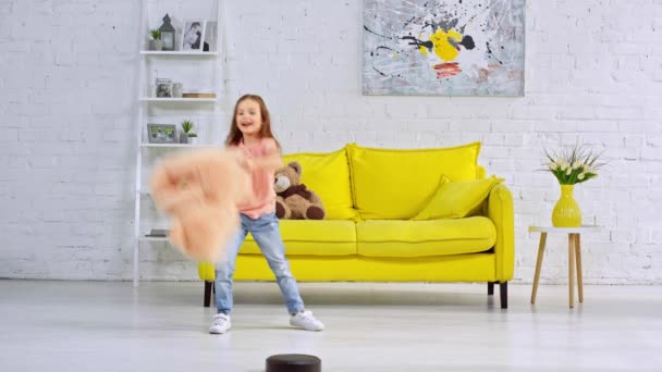 happy kid playing with soft toys near robotic vacuum cleaner - Imágenes, Vídeo