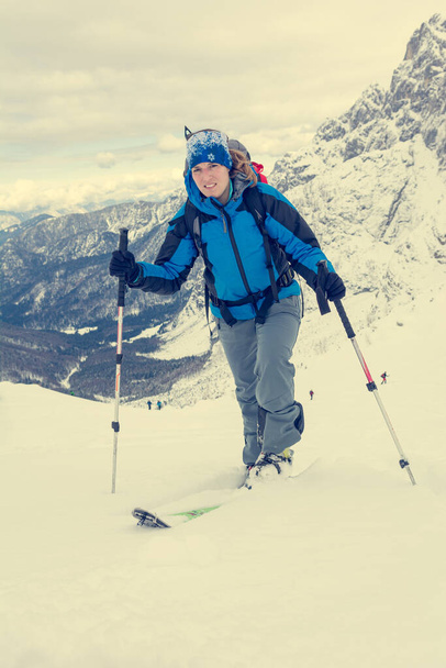 Female ski tourer ascending snow covered mountain slope. - Photo, Image