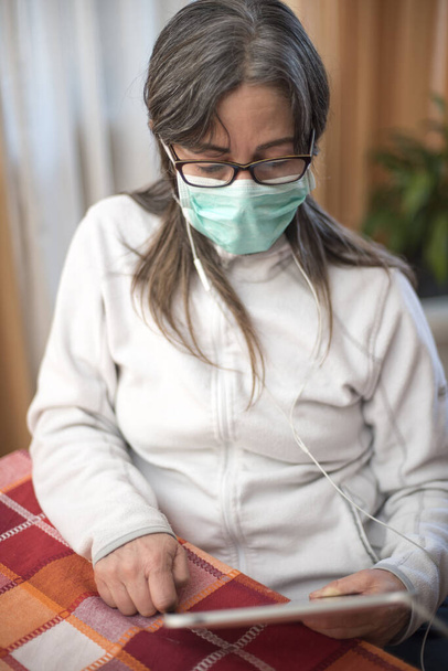 Vírus Corona. Mulher doente do vírus da corona lendo no comprimido, vestindo proteção respiratória de segurança e recuperação da doença em casa. Paciente isolado para prevenir infecção
 - Foto, Imagem