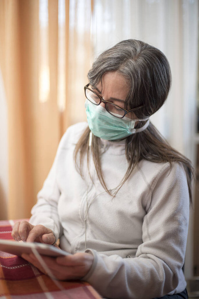 Coronavirus. Kranke Frau mit Coronavirus mit Tablette, trägt Atemschutz und erholt sich zu Hause von der Krankheit. Patient isoliert, um Infektionen zu verhindern - Foto, Bild