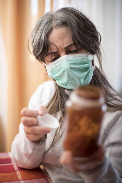 Het Corona Virus. Zieke vrouw van het corona-virus die ademhalingsbescherming draagt, met een container met medicijnen en herstel van de ziekte thuis. Patiënt geïsoleerd om infectie te voorkomen - Foto, afbeelding
