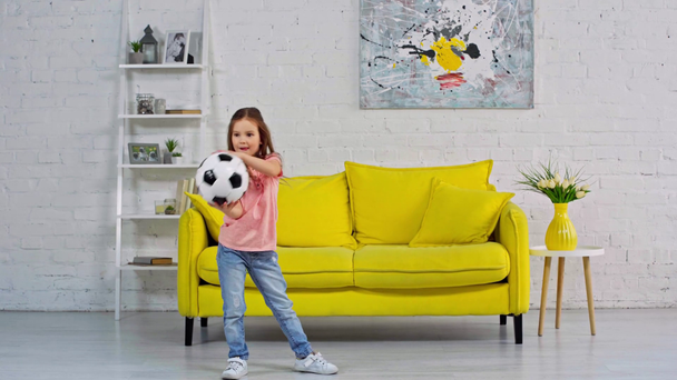 χαριτωμένο παιδί παίζει με μπάλα ποδοσφαίρου στο σαλόνι  - Πλάνα, βίντεο