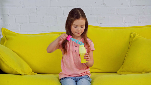 cute kid blowing soap bubbles while sitting on sofa  - Footage, Video