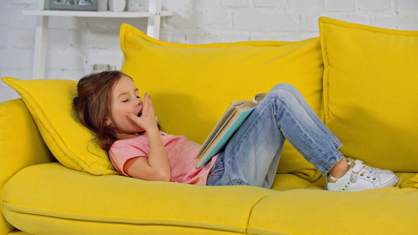 κουρασμένο παιδί χασμουριέται ενώ διαβάζει βιβλίο  - Πλάνα, βίντεο