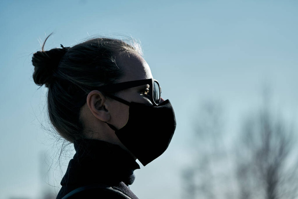Young girl in a black protective mask and black sunglasses on the street, protecting against the virus - Photo, image