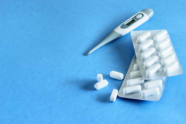 Thermomètre et paquets de pilules anti-inflammatoires sur le fond bleu gros plan. Anti-grippal, concept de sécurité
.  - Photo, image