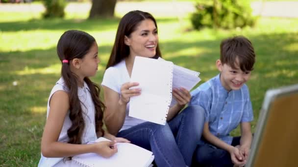Eine schöne Englischlehrerin unterrichtet mit zwei Kindern an einem Whiteboard eine Outdoor-Lektion in der Natur. der Lehrer blättert in den Notizen und lacht lustig mit den Kindern. - Filmmaterial, Video