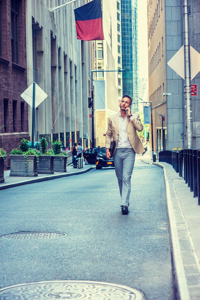 Empresario europeo viajando, trabajando en la ciudad de Nueva York, con barba, poco pelo gris, vistiendo chaqueta beige, pantalones grises, zapatos de cuero, portafolios, caminando por la calle, hablando por teléfono celular - Foto, Imagen