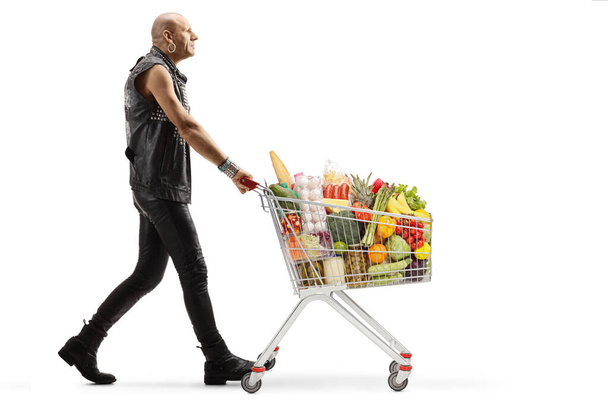 Full length profile shot of a bald punk walking with a shopping cart full of food isolated on white background - Foto, Bild