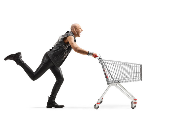 Full length profile shot of a punk running with an empty shopping cart isolated on white background - Φωτογραφία, εικόνα