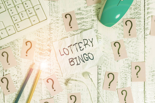 Text sign showing Lottery Bingo. Conceptual photo game of chance in which each player matches numbers printed Writing tools, computer stuff and scribbled paper on top of wooden table. - Photo, Image