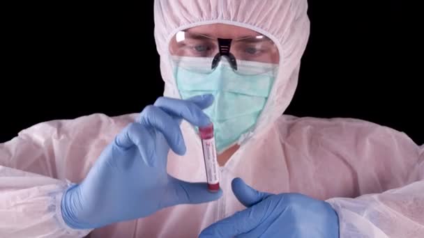Man in professional white safety uniform is watching and showing test-tube with positive Coronavirus blood test with biohazard label. Covid-19 pandemic. World pandemic. - Video, Çekim