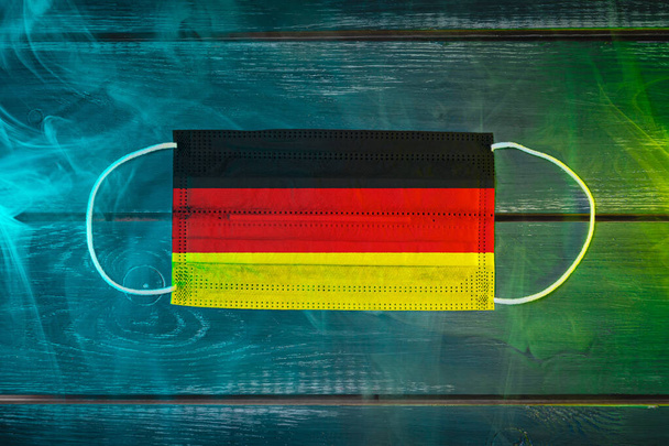 Orvosi maszk a levegőben terjedő betegségek ellen, festett a nemzeti zászló Németország egy fekete háttér kék-zöld füst. Orvosi védelem a levegőben terjedő betegségek, coronavirus ellen - Fotó, kép