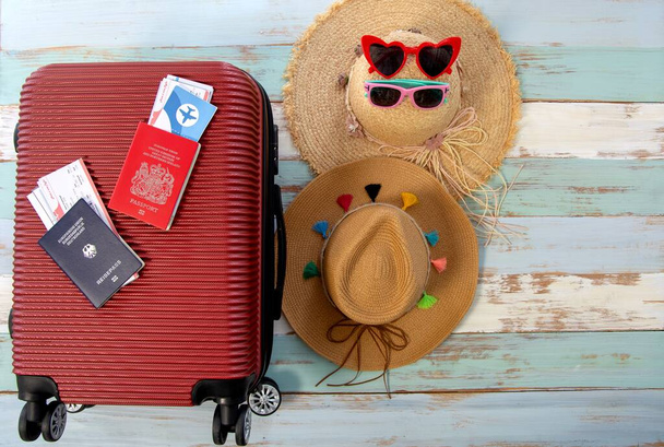 Επίπεδη lay βαλίτσα, γυαλιά ηλίου, και καπέλα σε κόκκινο φόντο βαλίτσα ελάχιστη δημιουργική έννοια καλοκαιρινές διακοπές ταξίδια - Φωτογραφία, εικόνα