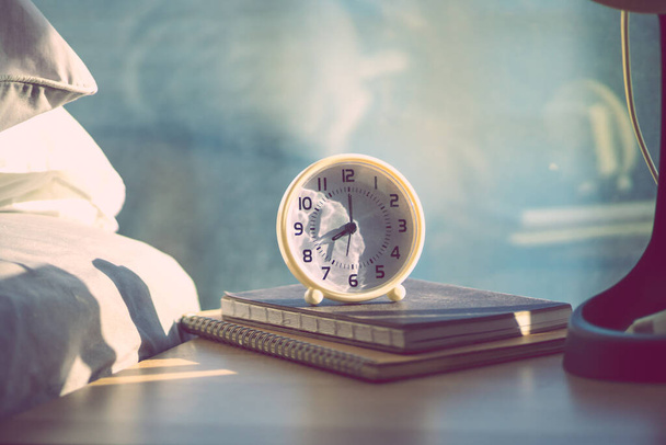 cerrar u reloj despertador blanco 8 oclock am, en la mesa de madera cerca de la cama con luz cálida de la mañana de la ventana, color vintage con espacio de copia
 - Foto, Imagen