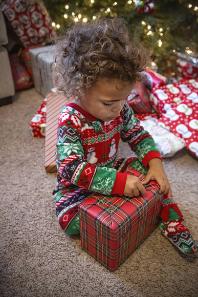 Aranyos fekete kisfiú, karácsonyi ajándékot csomagol ki karácsony reggelén.. - Fotó, kép