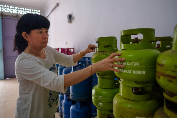 Asiatische indonesische Frauen arrangieren 3Kg-Gasflaschen in einem kleinen Geschäft in Familienbesitz, auch Warung genannt. Die Übersetzung des Textes lautet "nur für die Armen". Selektiver Fokus. - Foto, Bild