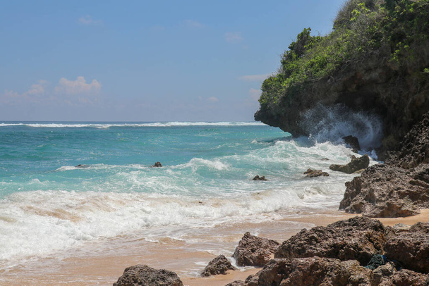 Pantai Gunung Payung ranta hienolla kultahiekalla, Bali. Turkoosin sininen vesi muuttuu merivaahdoksi, kun aallot murtuvat rannikon kallioita vasten. Aurinkoinen päivä sinisellä taivaalla. Turisti luonnollinen käsite
. - Valokuva, kuva