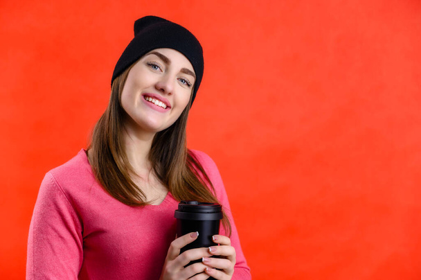 Portrait of a pretty smiling Caucasian woman in a pink sweater on a red background. The model stands in front of the camera in a black hat with different emotions. - Valokuva, kuva