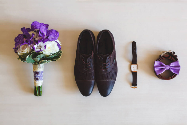 Wedding shoes, belts, watches and bouquet on a white surface. Accessories for the groom on the wedding day. - Foto, Bild