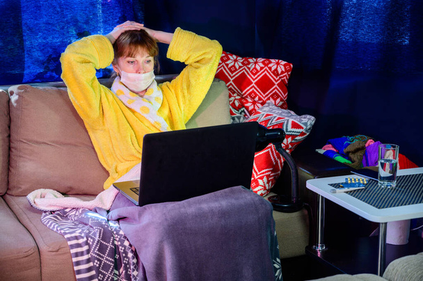 Foto de una mujer en una máscara en el interior de un hogar bajo cuarentena. El modelo funciona, utiliza un ordenador portátil a través de Internet
. - Foto, Imagen