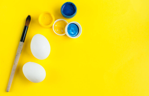 series for a master class on egg painting. Easter master class. Step 1. ingredients. white eggs on a yellow background with blue and yellow paint - Foto, Imagen