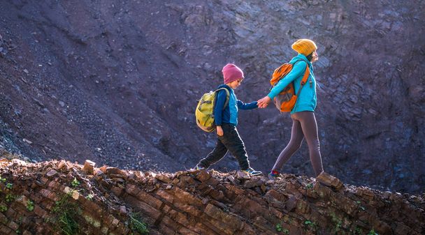 Μια γυναίκα και το παιδί της περπατούν σε ένα ορεινό μονοπάτι. Ένα αγόρι με σακίδιο ταξιδεύει με τη μητέρα του. Πεζοπορία με παιδιά. Το παιδί περπατάει μέσα στο δάσος. Ενεργές καλοκαιρινές διακοπές.  - Φωτογραφία, εικόνα