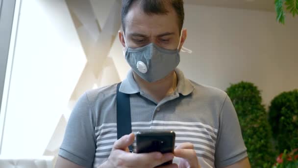 Man in Healthy Face Mask with Smartphone sitting in Shopping Mall - Filmagem, Vídeo