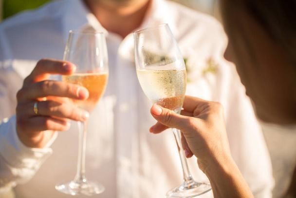 Champagne glasses in the hands of the bride and groom at sunset. - Foto, Imagen