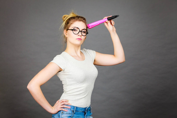 Student looking woman wearing nerdy eyeglasses holding big oversized pencil thinking about something. - 写真・画像