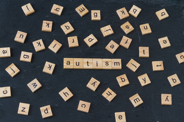 Autizmus betűzött fa betű blokkok betűkkel véletlenszerűen elterjedt a kép körül sötét pala háttér. - Fotó, kép