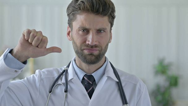 Vážný mladý doktor ukazující palce dolů - Fotografie, Obrázek