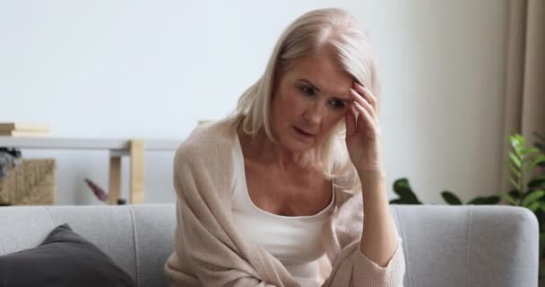Frustrated mature old female retiree sitting on couch, feeling anxious. - Πλάνα, βίντεο