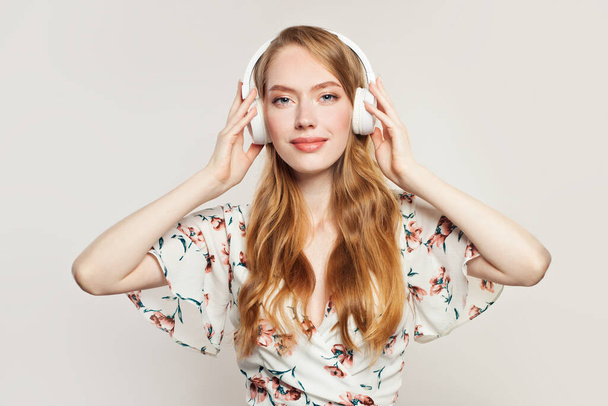 Iloinen punapää nainen kuulokkeet valkoisella taustalla
 - Valokuva, kuva