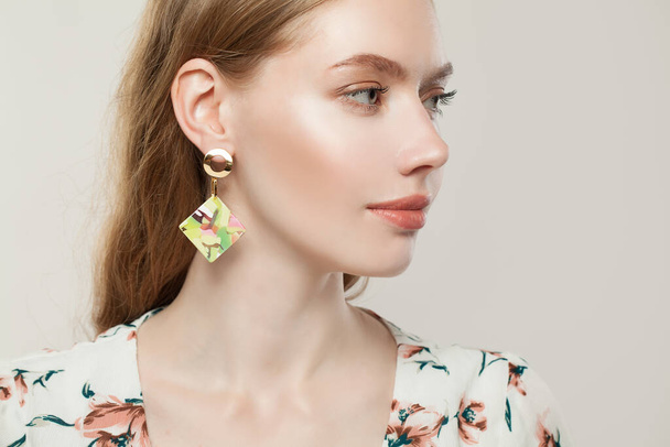 Beautiful young woman with golden earrings on white, profile - Valokuva, kuva