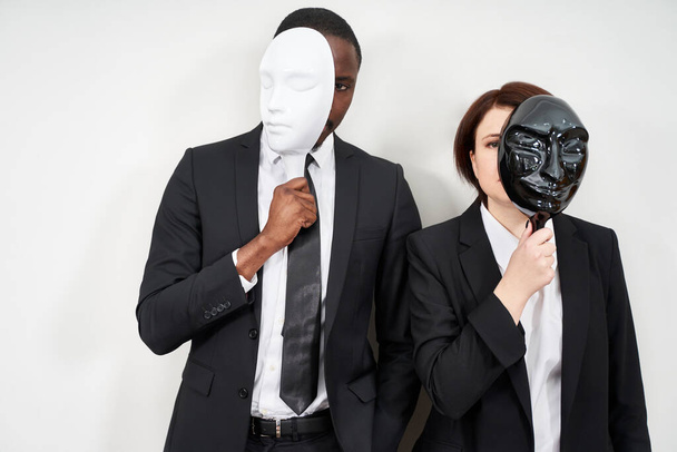 Homme africain et femme caucasienne portant des costumes noirs cachant visage avec des masques en plastique
 - Photo, image