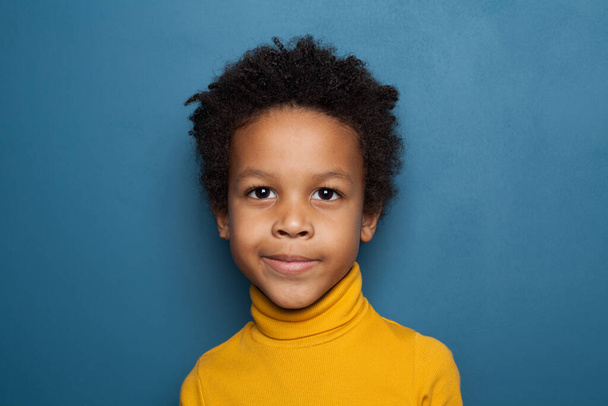 Ciekawy czarny chłopiec uśmiecha się na niebieskim tle - Zdjęcie, obraz