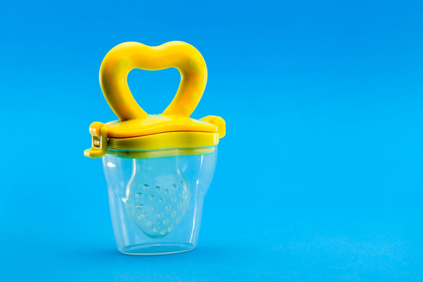 Fruit feeder in a plastic case with a yellow handle and a silicone pacifier on a blue background with a copy space. - Foto, Bild