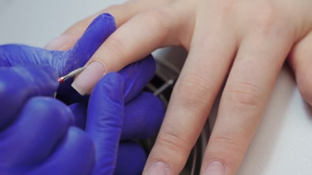 美容室で青手袋の女性マニキュアマスターはマニキュアマシンを使用してクライアントの爪にキューティクルを処理します. - 映像、動画