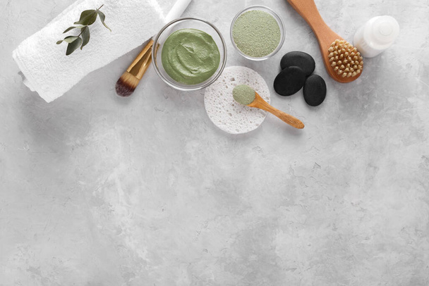 Cosmetic green clay powder for skin and hair, spa and wellness, natural cosmetics, towel sponge and brushes on light grey background with copy space - 写真・画像