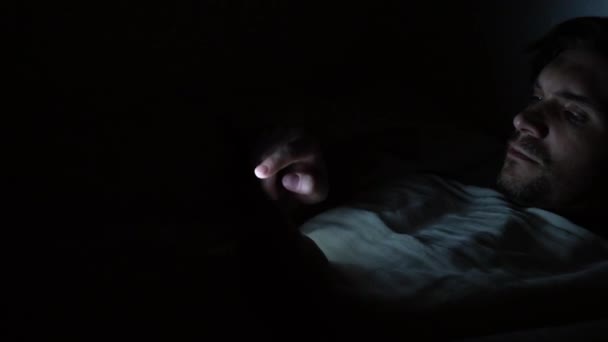 Young man in bed at night uses a smartphone. Insomnia and digital dependence, the girl in bed - Materiał filmowy, wideo