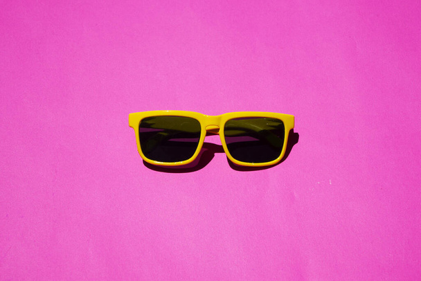 Gelbe Sonnenbrille mit Muster auf rosa Pastellgrund. Minimales Sommerkonzept. Isometrischer Druck. - Foto, Bild