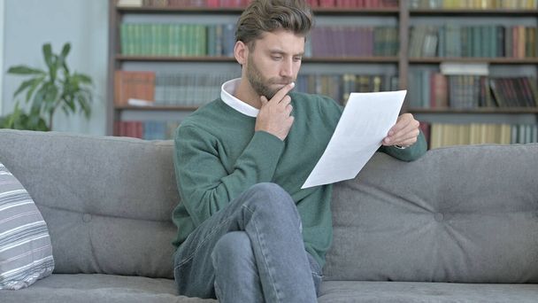 Nachdenklicher Mann sitzt auf Sofa und studiert Dokumente - Foto, Bild
