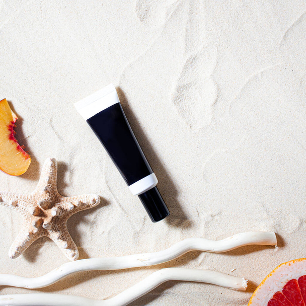 Safe sun. Skin care. A tube of cream lies on the beach sand, surrounded by vibrant fruits, corals, and palm leaves. - Foto, Bild