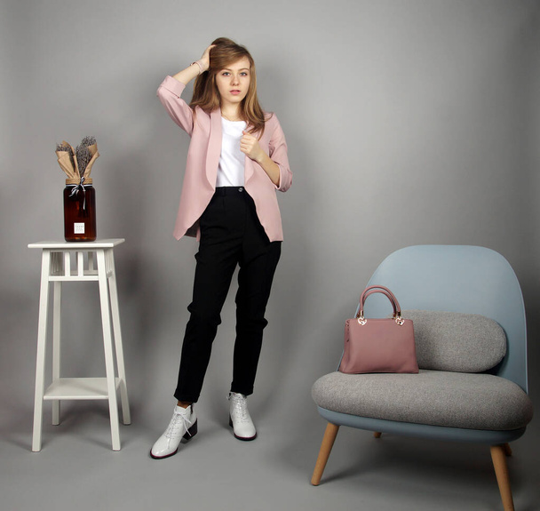 Pretty young blonde european girl at pink coat posing on camera.studio shooting at grey background - Fotó, kép